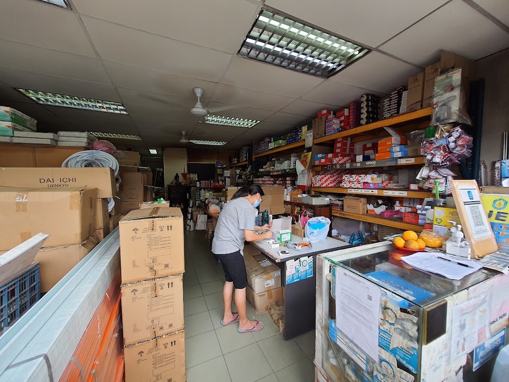 Narrow electrical shop interior with stocked shelves on the right, a glass counter and stacked cartons on the left
