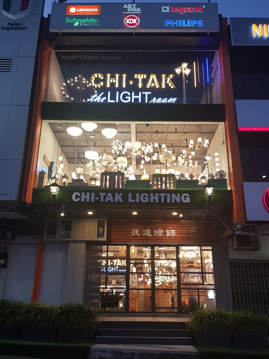 Three-storey lighting showroom with a lit "Chi-Tak the Light Room" sign, glass upper floor full of pendant lights and a brand-logo signboard on top