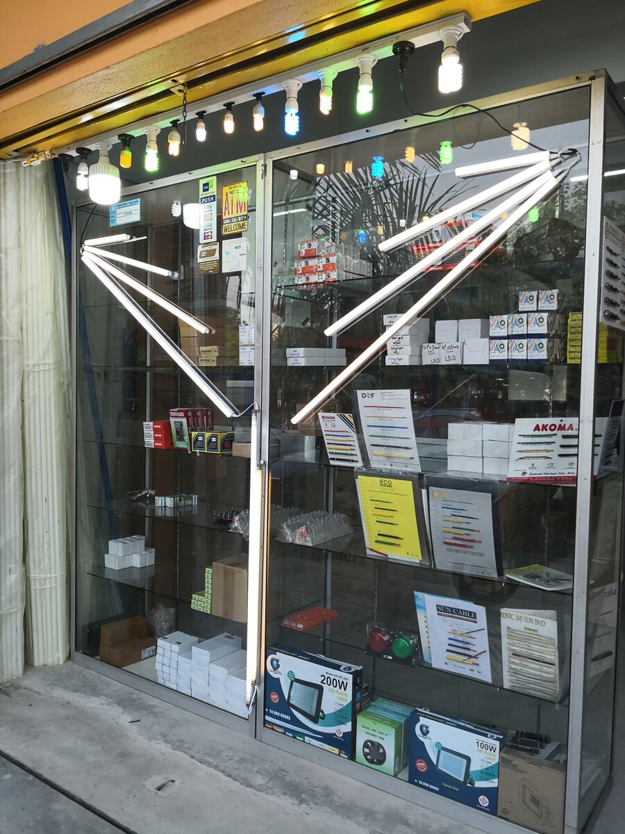 Glass display cabinet at a shopfront with lit LED tubes fanned across the glass, lamps hanging above, and boards showing coloured single-core wire samples on the shelves