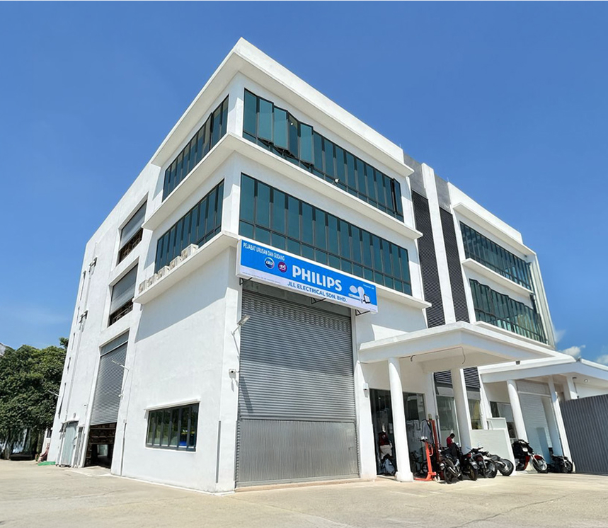 White multi-storey office and warehouse building with blue-tinted windows and a blue Philips signboard over a roller shutter, with a porch entrance to the right, under a clear blue sky