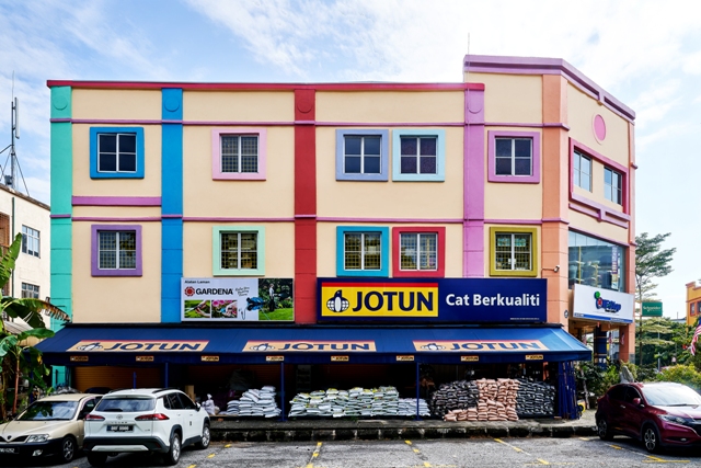 Colourful three-storey shop building with a blue Jotun Cat Berkualiti signboard and sacks stacked under the awning