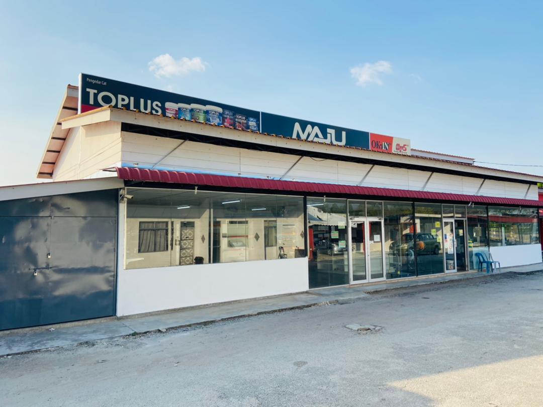 Long white single-storey shop with a glass front and a roof-line signboard reading Toplus, MAJU and OK-IN under a blue sky