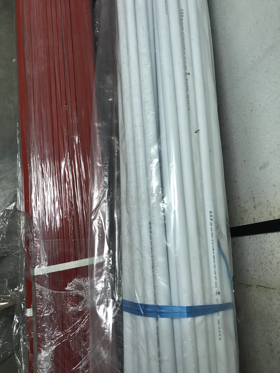 Long white PVC conduit pipes strapped in a bundle next to a bundle of red lengths, leaning against a wall