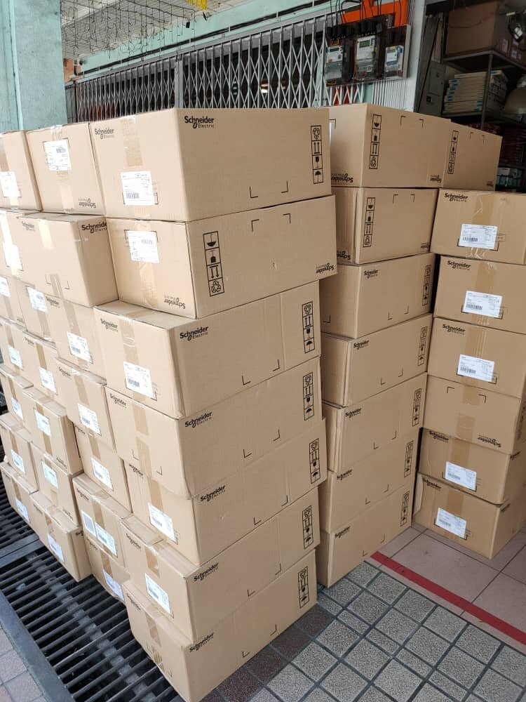 Stacks of brown cardboard cartons printed with the Schneider Electric logo stacked in front of a shop's folding gate