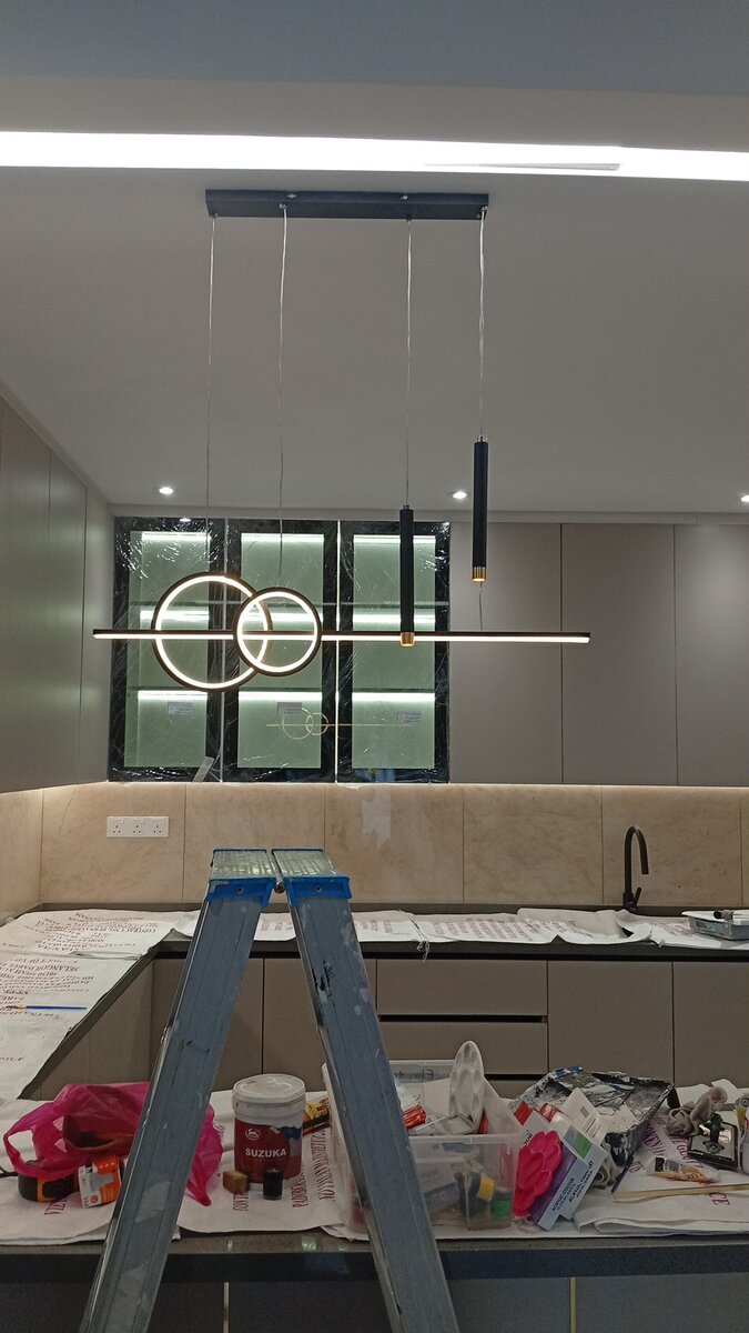 Renovated kitchen with a step ladder in front of a counter, a ring pendant light and slim hanging lights over it, and cabinets with lit glass shelves behind