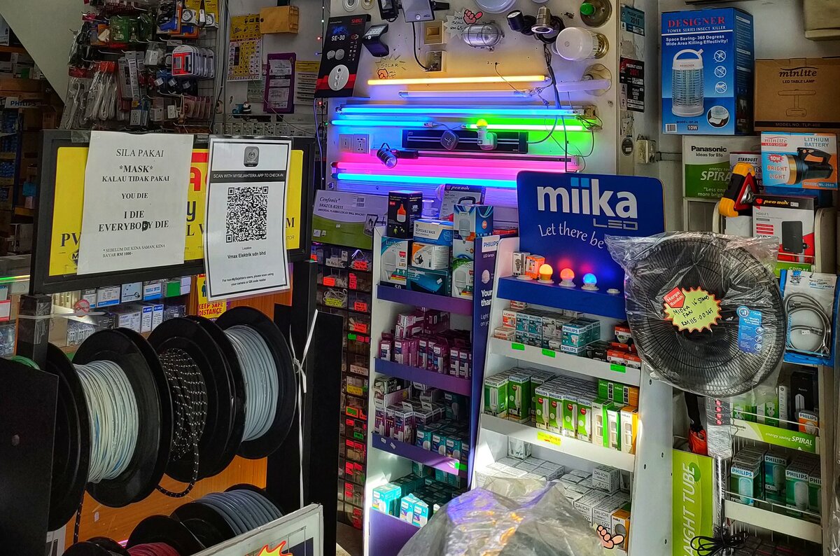 Cable reels on a stand in front of a wall of lit fluorescent and LED fittings, a Philips LED lamp stand, a blue Miika LED display with Philips lamp boxes and a wrapped stand fan