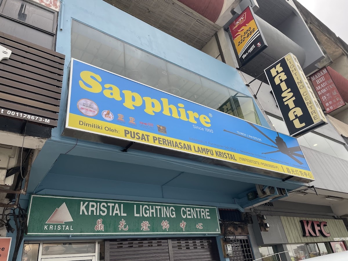 Two-storey shop lot with a large blue and yellow Sapphire fan signboard above a green Kristal Lighting Centre sign with Chinese characters, and a vertical black Kristal sign at the corner