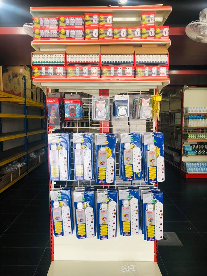 Display stand with red boxes of circuit breakers on the top shelves and hanging packs of white extension sockets and meters below