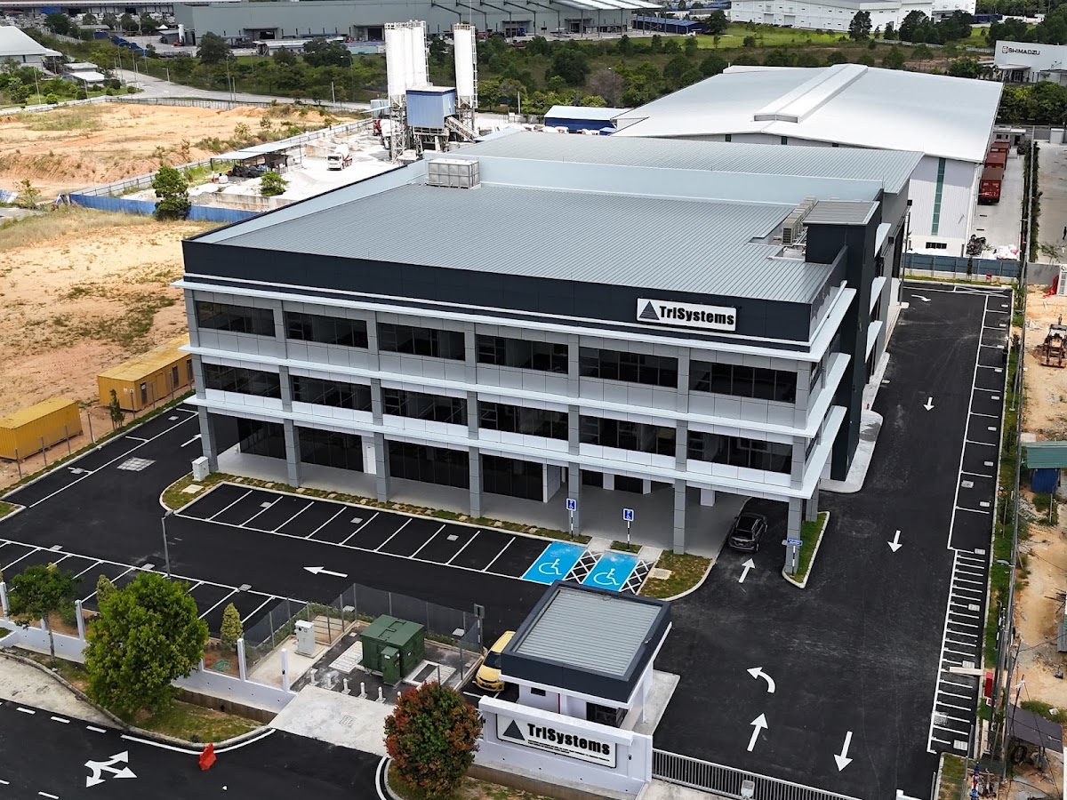 Aerial view of a three-storey grey office block with a TriSystems sign, car park and an industrial building behind