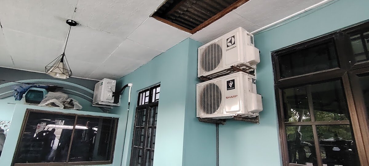 Outdoor air-conditioner compressor units stacked on brackets on a pale green wall under a porch ceiling