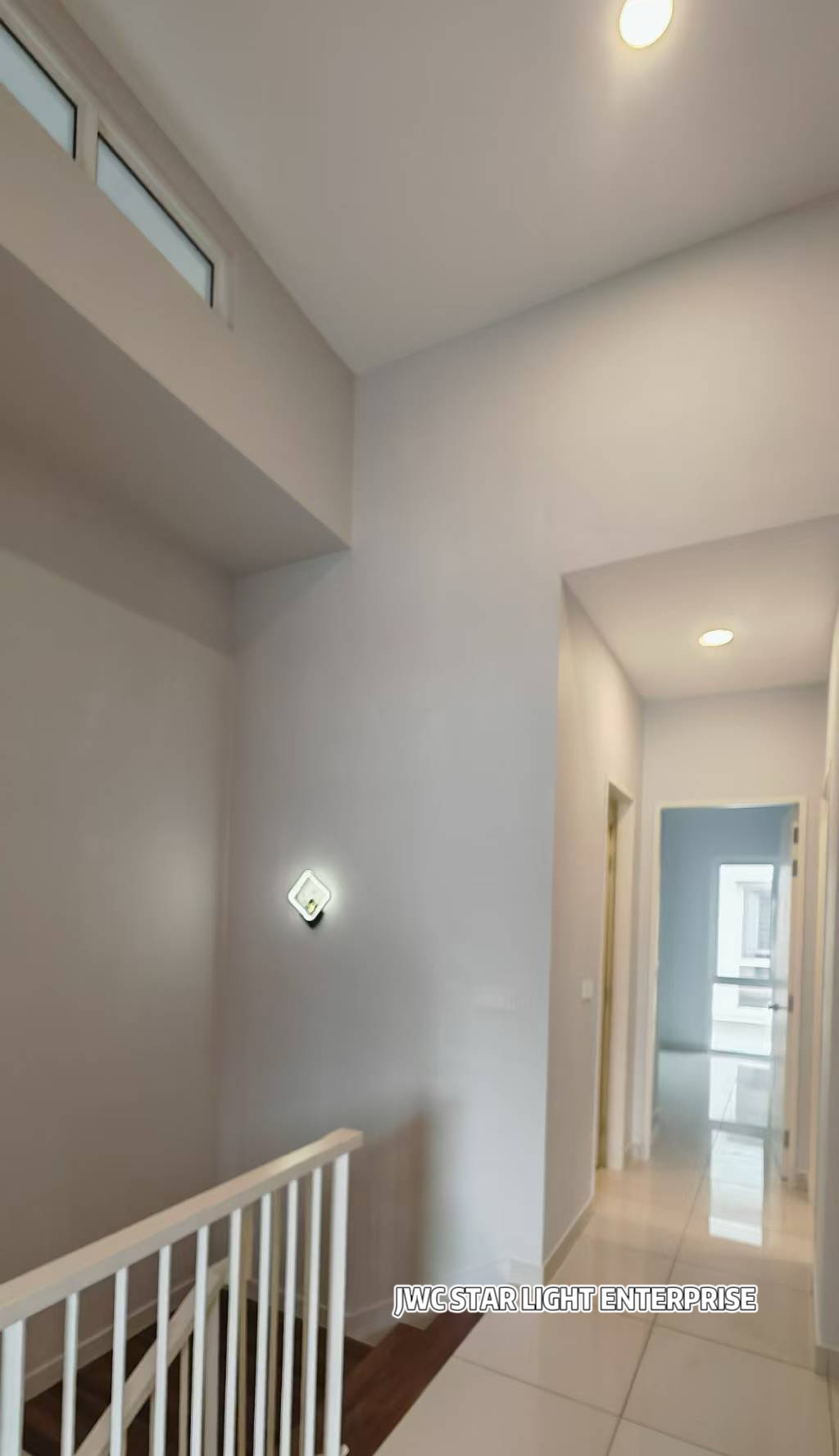 Upstairs landing with white stair railing, a small square wall light and round recessed ceiling downlights, with a corridor and doorways beyond