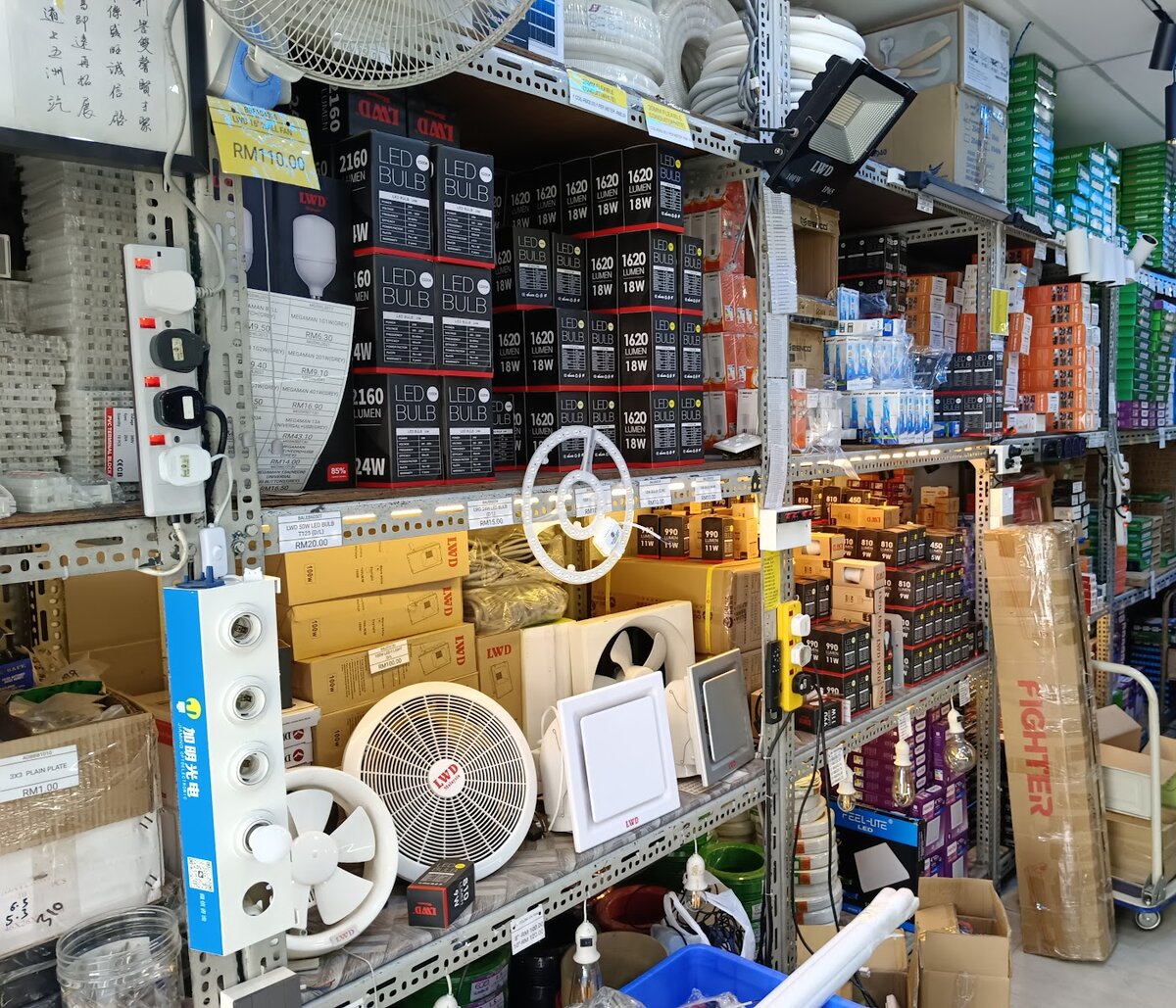 Metal shelving packed with black and red LWD LED bulb boxes, white exhaust fans and a round wall fan, a floodlight, power strips and a tall Fighter carton