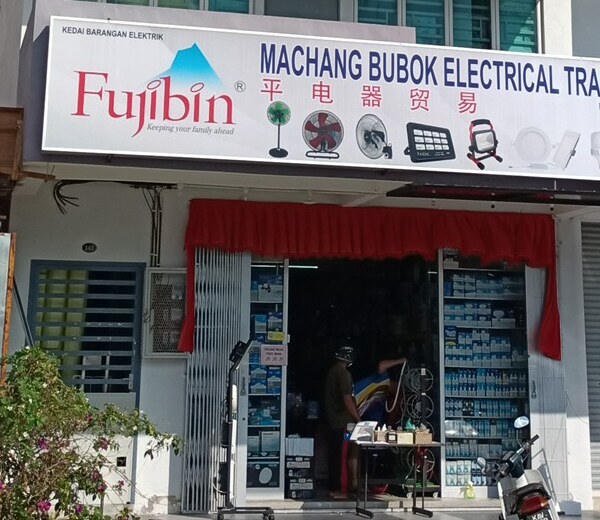 Shopfront with a white Fujibin and Machang Bubok Electrical Trading signboard over an open door and shelves of boxed electrical goods