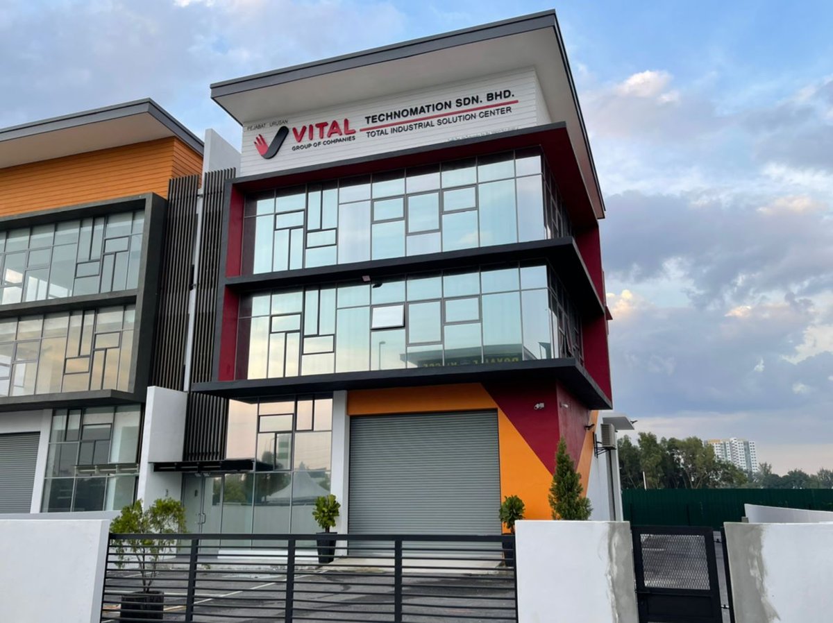Three-storey red, orange and grey corner building with glass windows, a roller shutter and a sign reading Vital Group of Companies, Technomation Sdn. Bhd., Total Industrial Solution Center
