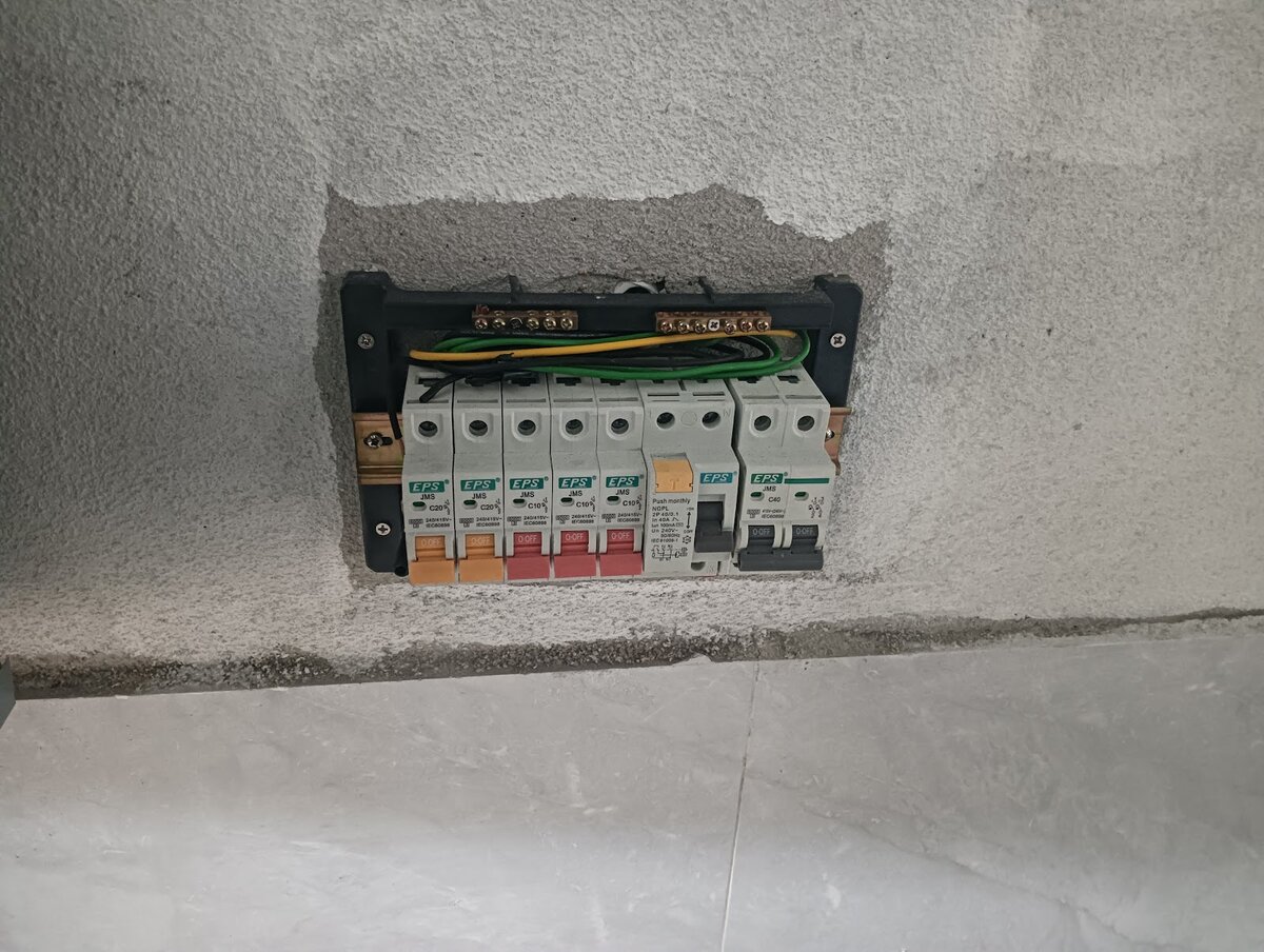 Distribution board set into a rough plastered wall opening, with five EPS miniature circuit breakers, an RCCB with a yellow test button and a double-pole main switch