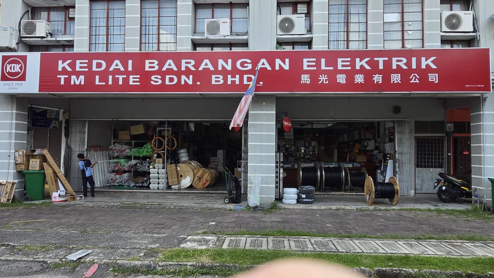 Double-unit shopfront with a red TM Lite Sdn Bhd signboard and cable drums and conduit stacked at the open entrance