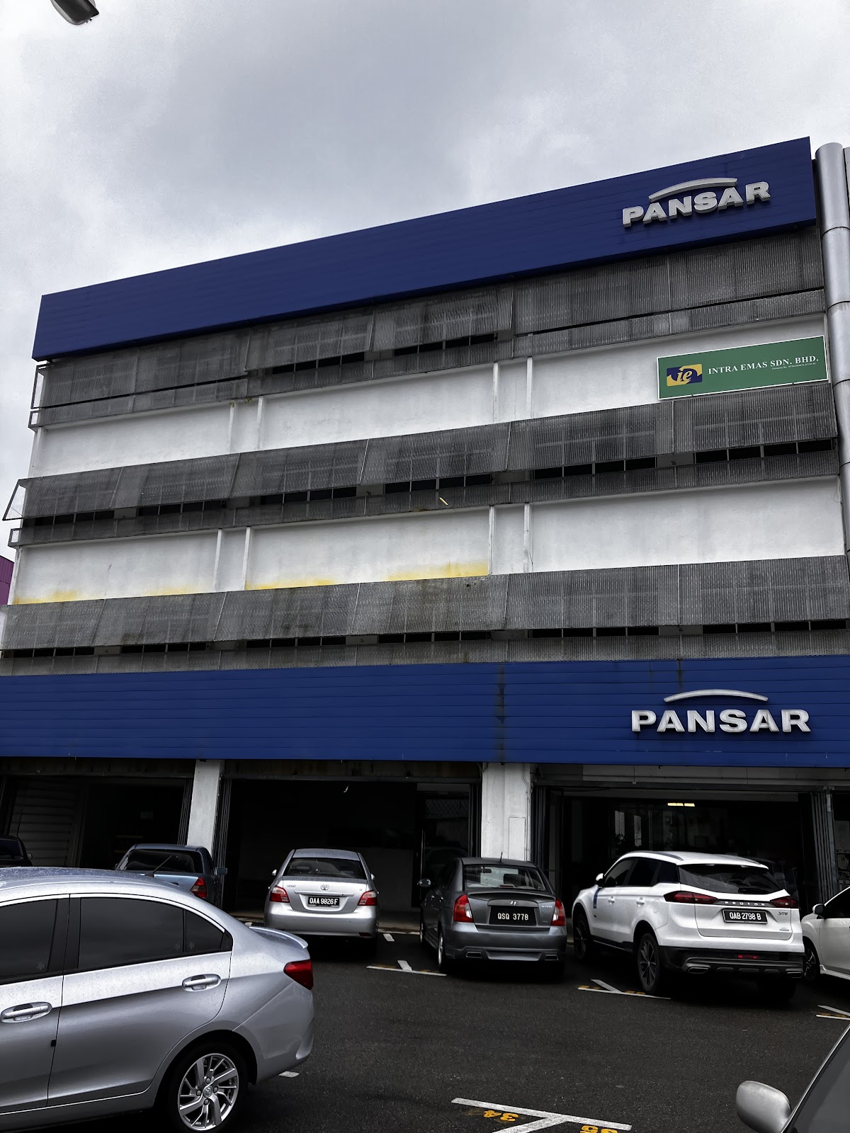 Four-storey building with blue PANSAR signage at the top and above the ground-floor bays, cars parked in front