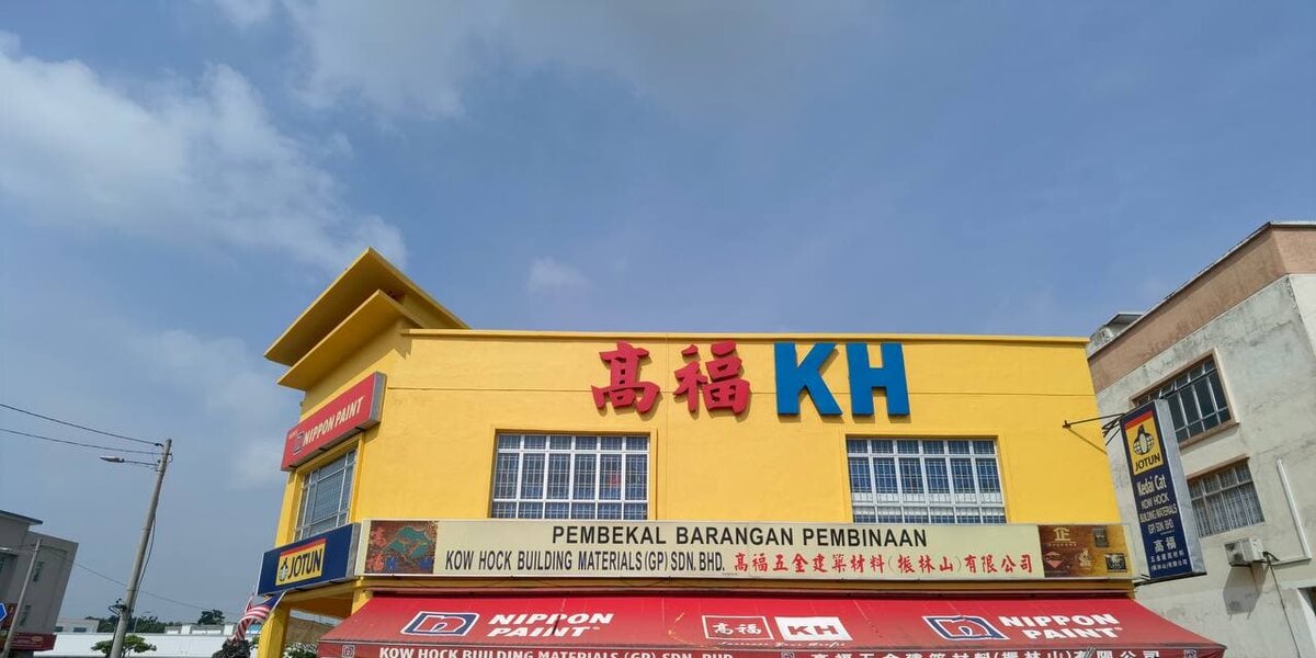Yellow two-storey corner shop with a large "高福 KH" sign, a Kow Hock Building Materials (GP) signboard and red Nippon Paint awnings