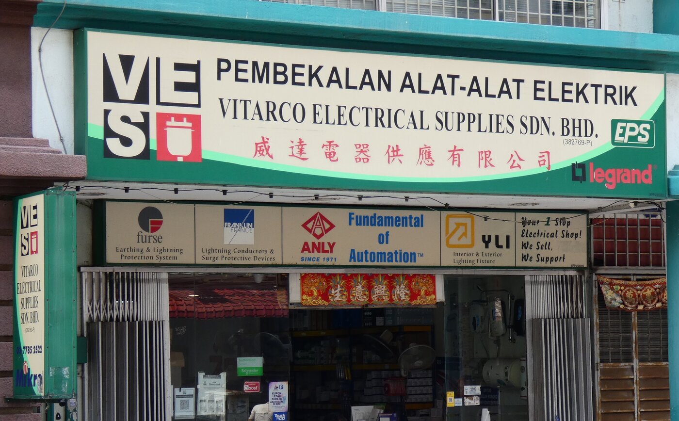Green and cream shop signboard reading Pembekalan Alat-Alat Elektrik, Vitarco Electrical Supplies Sdn. Bhd. and Chinese characters, above a row of brand panels and a glass shopfront
