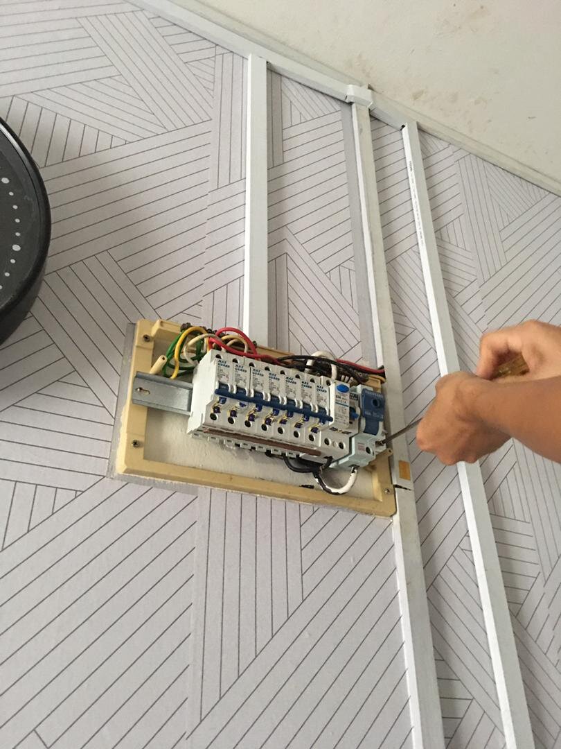 Hand with a screwdriver working on a row of circuit breakers in an open distribution board on a wall