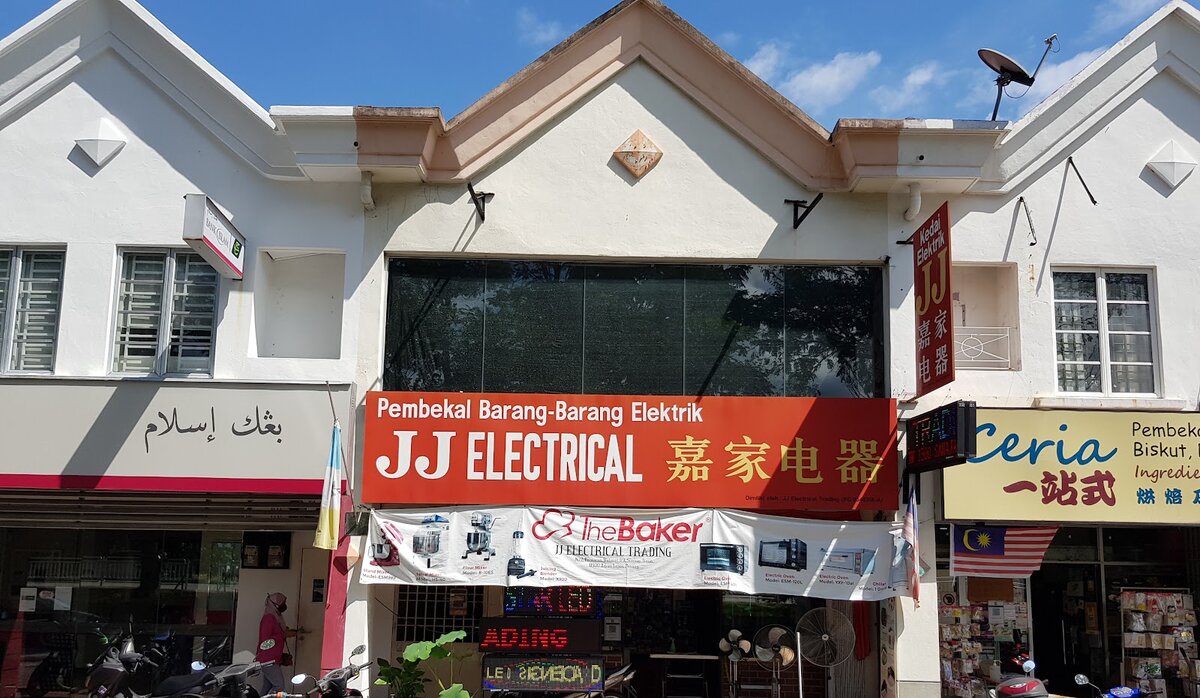 Red JJ Electrical signboard on a white two-storey shophouse, with a bakery-equipment banner and stand fans at the entrance