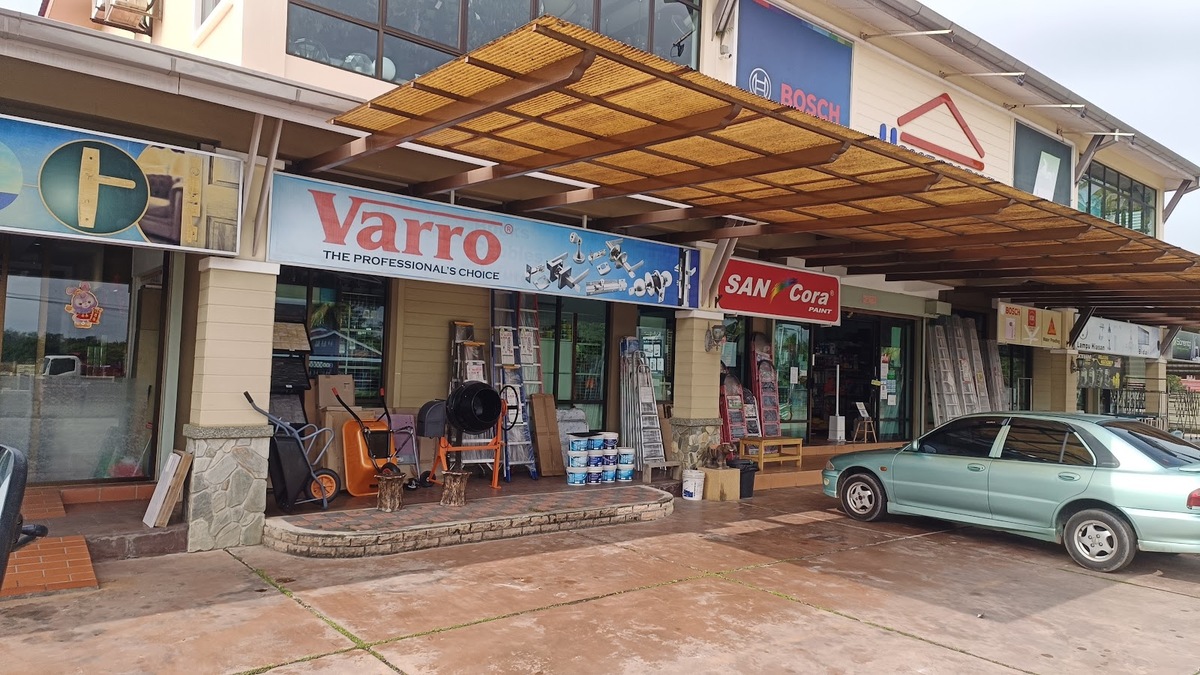 Row of shop units under a pergola, with a Varro door-hardware signboard, a San Cora sign, a Bosch panel and hardware goods displayed on the walkway
