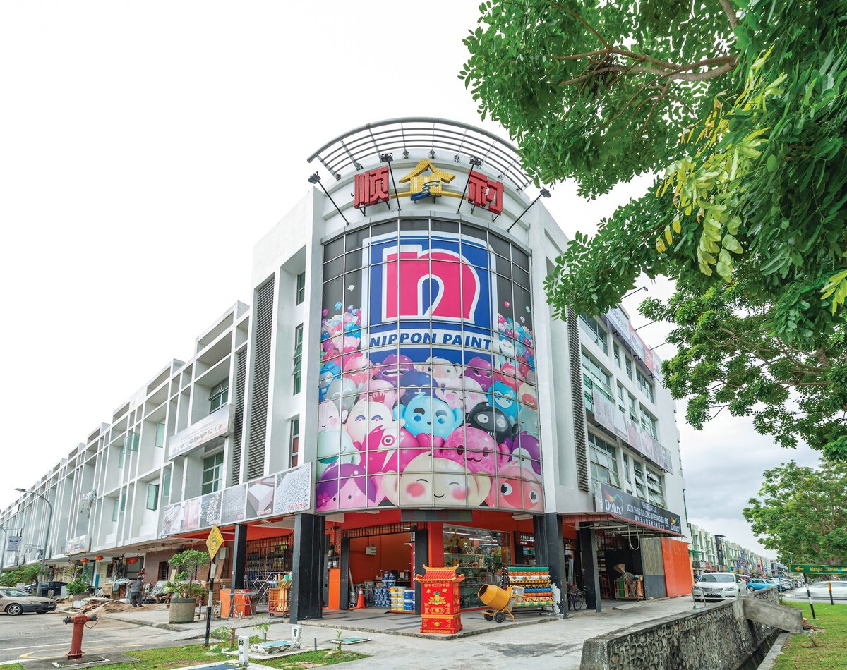 White corner shop building with a curved glass front covered by a large Nippon Paint mural and a red 顺衬 sign on top
