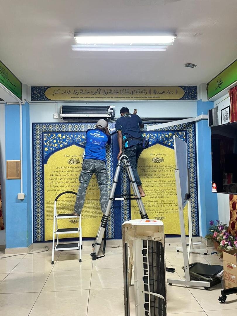 Two technicians in blue shirts on ladders working on an air-conditioner unit high on a wall