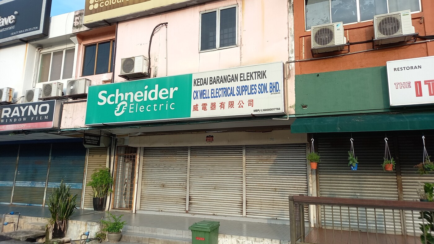 Two-storey shophouse with a green Schneider Electric and white CK Well Electrical Supplies signboard over closed shutters