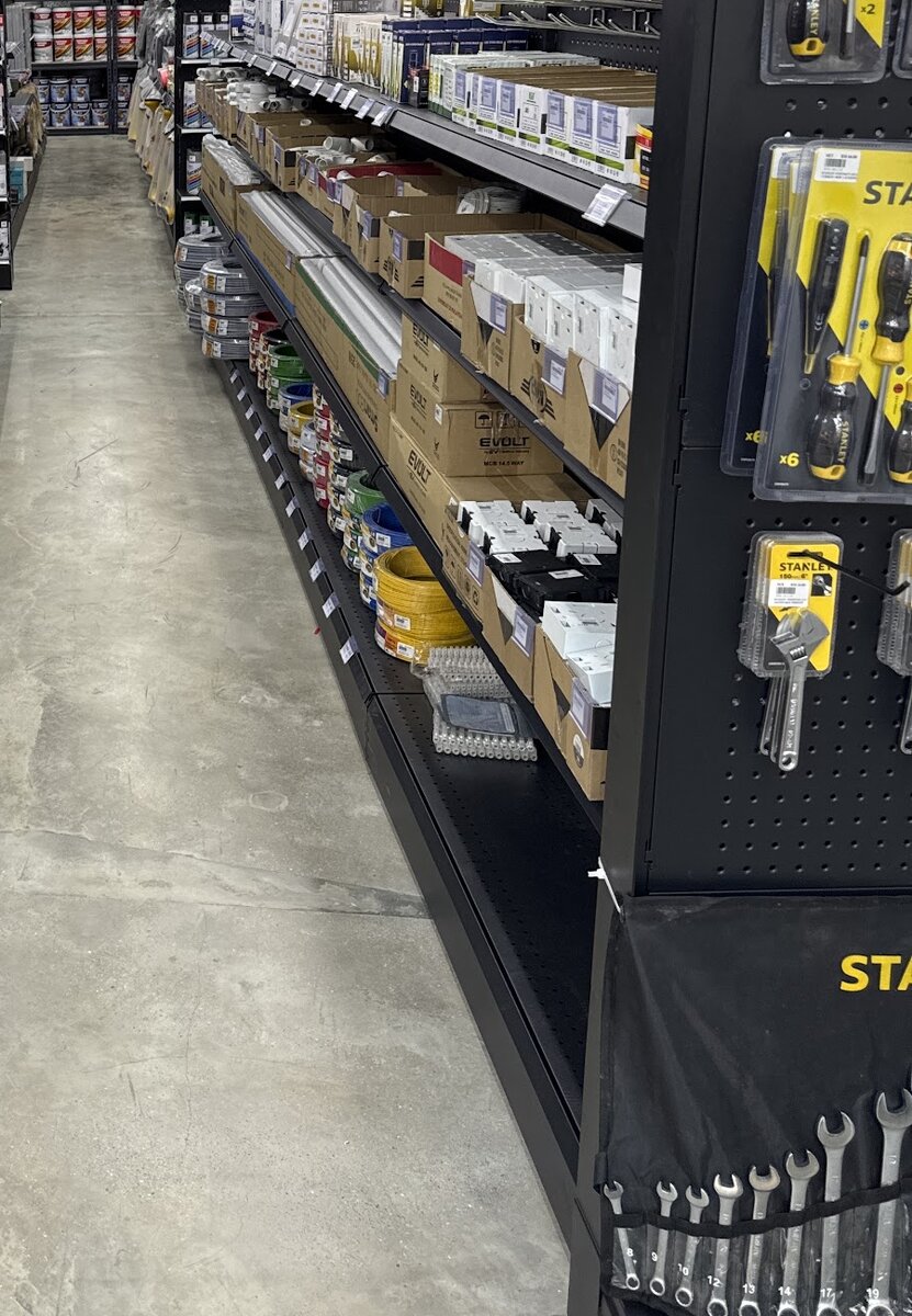Shop aisle with coils of coloured single-core cable on the bottom shelf, boxed distribution boards and white switch plates above, and a Stanley tool display on the right