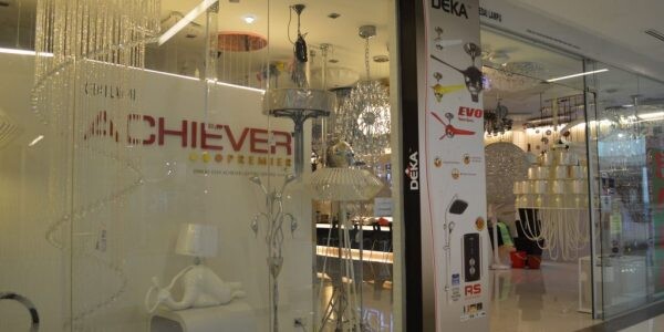 Glass shopfront with the Achiever Premier logo, hanging crystal chandeliers and lamps, and a tall Deka fan and water-heater banner on a pillar