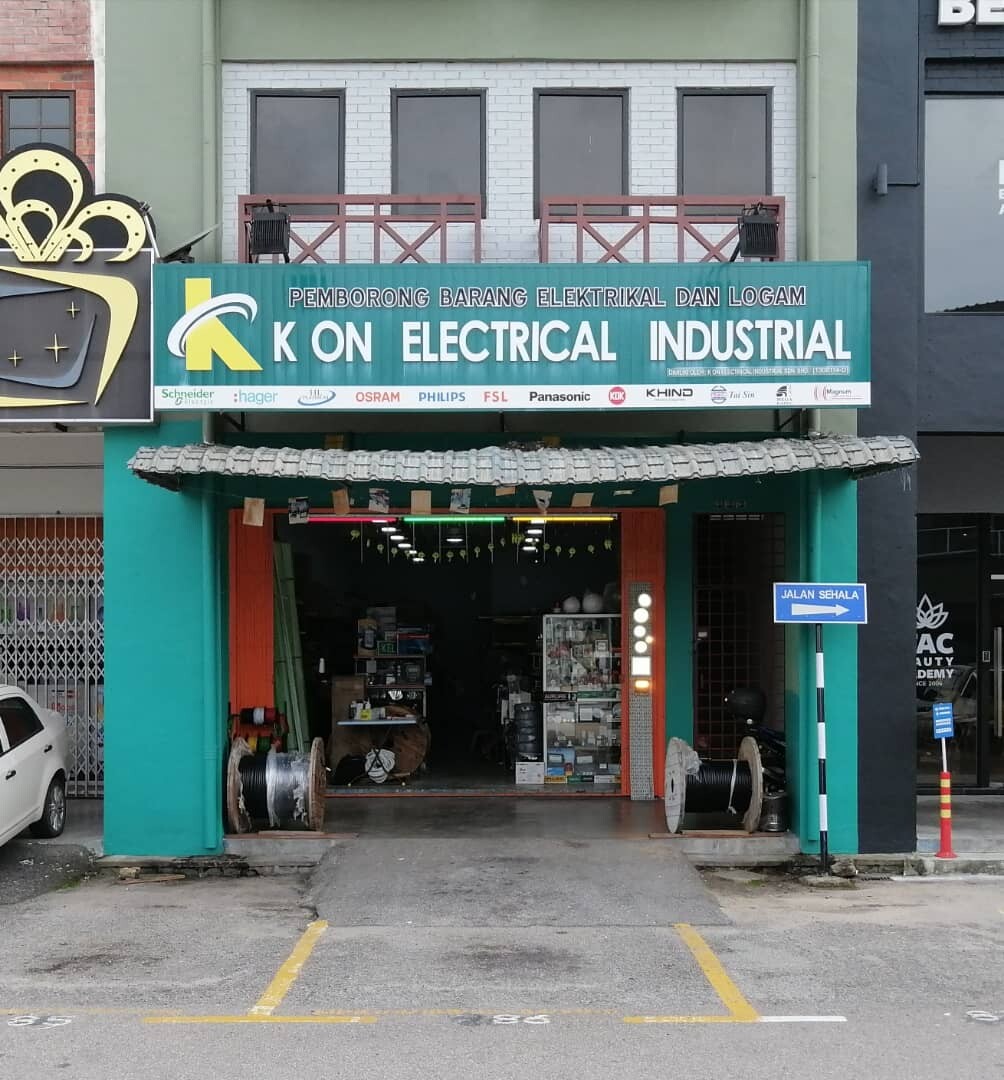 Shopfront with a green signboard reading K On Electrical Industrial, a strip of brand logos underneath, cable drums at the entrance and shelves of electrical stock inside