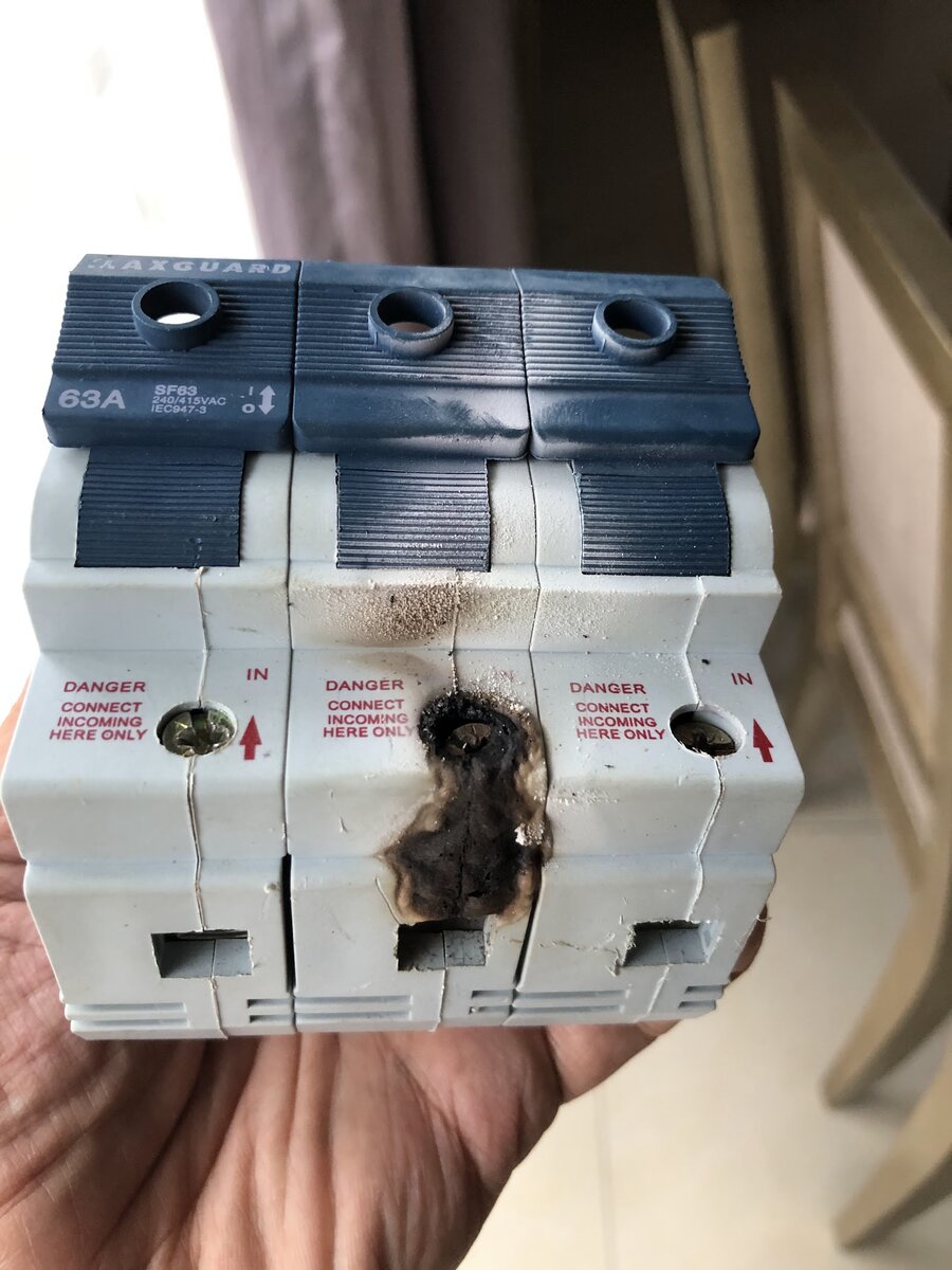 Hand holding a three-pole 63 amp isolator with blue toggles, the middle pole's housing burnt black