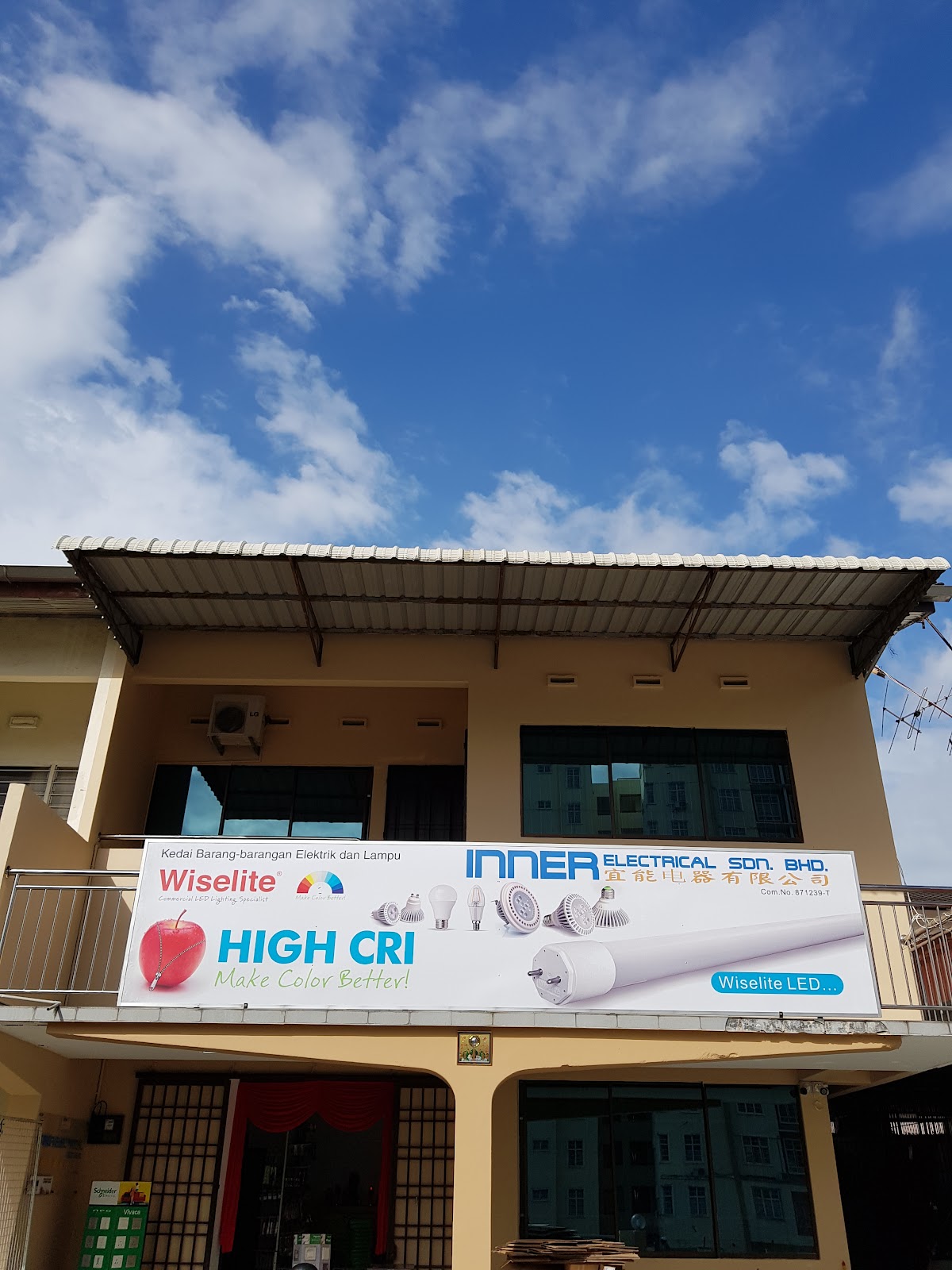 Two-storey terrace house with a large Inner Electrical and Wiselite High CRI signboard on the balcony under a blue sky