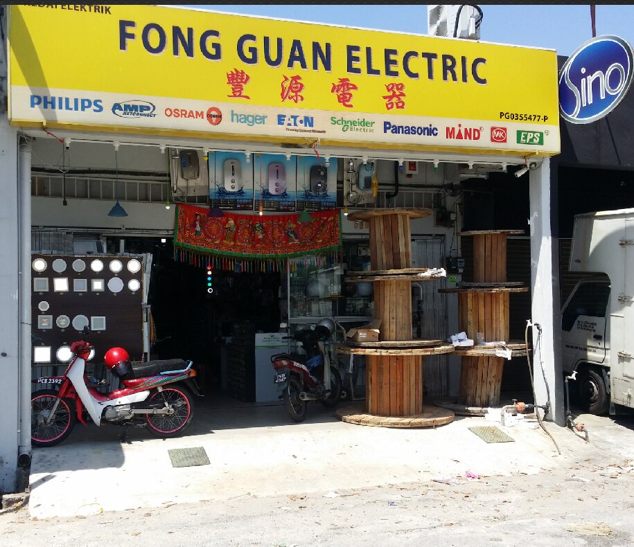 Yellow shop sign reading Fong Guan Electric 豐源電器 above an open shopfront with wooden cable drums, a board of round and square LED downlights, water heaters displayed above the entrance, and a blue Sino sign at the side