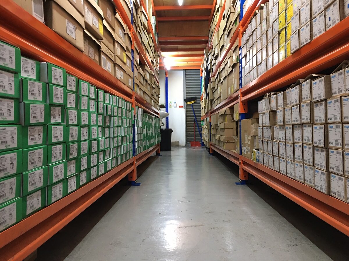 Warehouse aisle with orange racking full of green Schneider Electric boxes on the left and brown cartons on the right