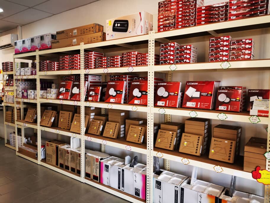 Rows of cream metal shelves stacked with red and brown boxes of LED downlights, with handwritten labels on the shelf edges