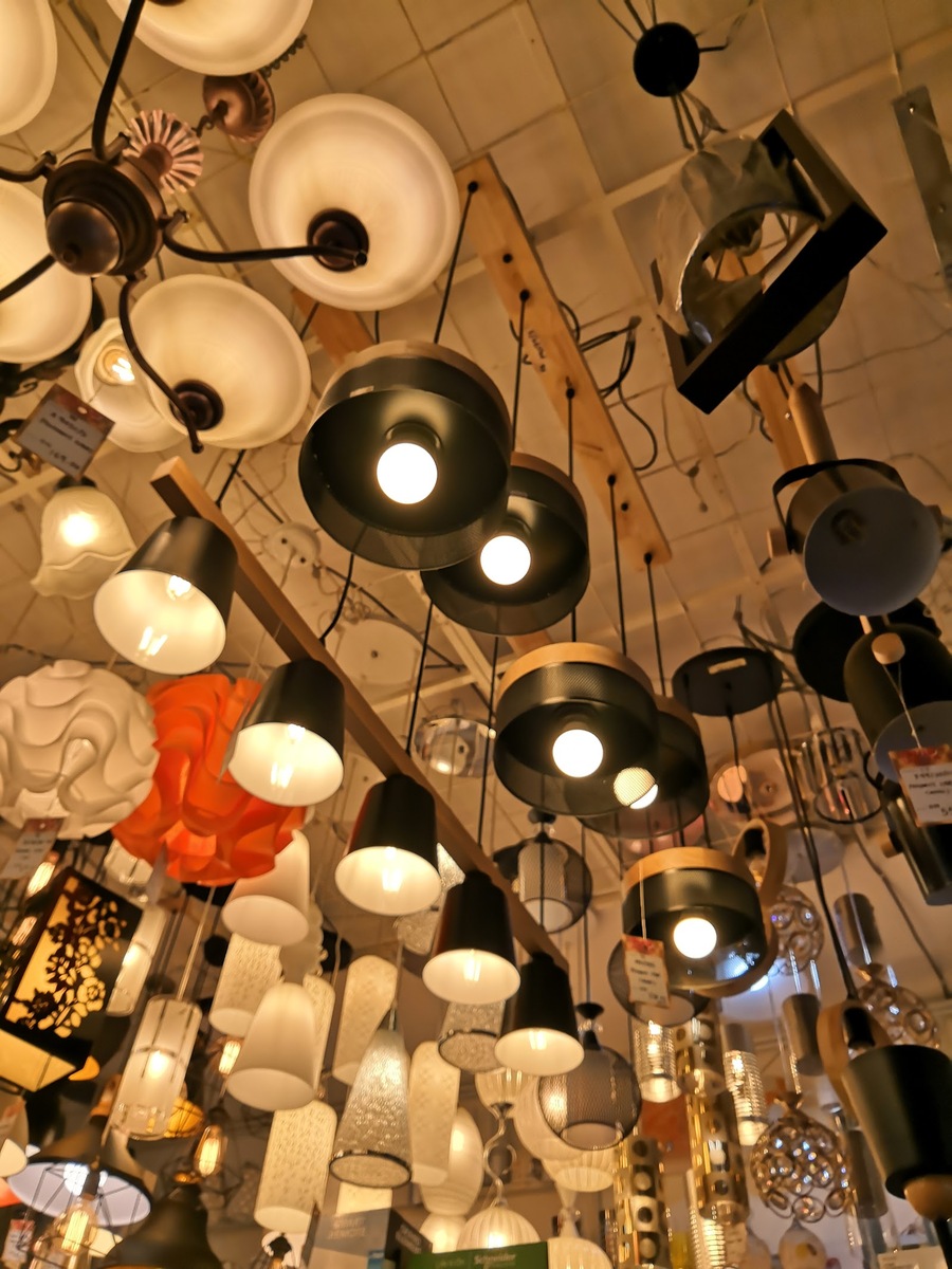 Dozens of pendant lamps, black shades, glass and orange lanterns hanging close together from a shop ceiling