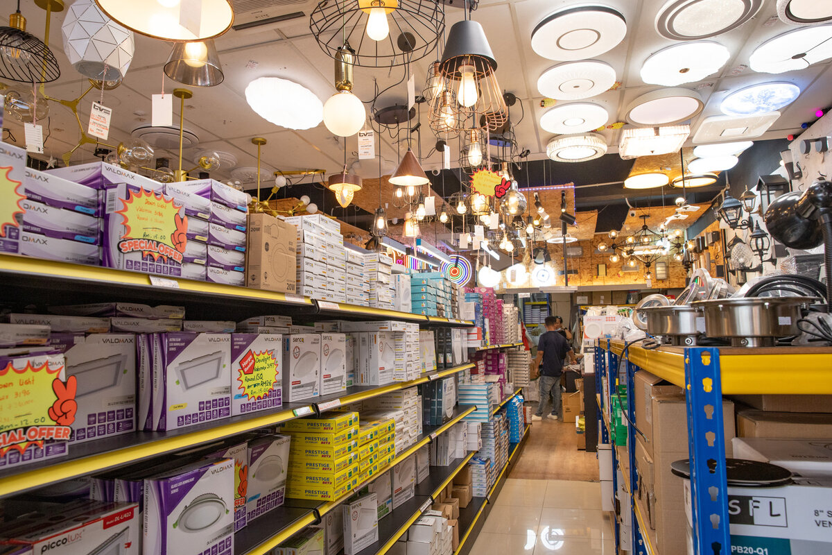 Shop aisle with shelves of purple and white LED downlight boxes, orange special-offer tags, and many pendant lamps and round ceiling lights overhead