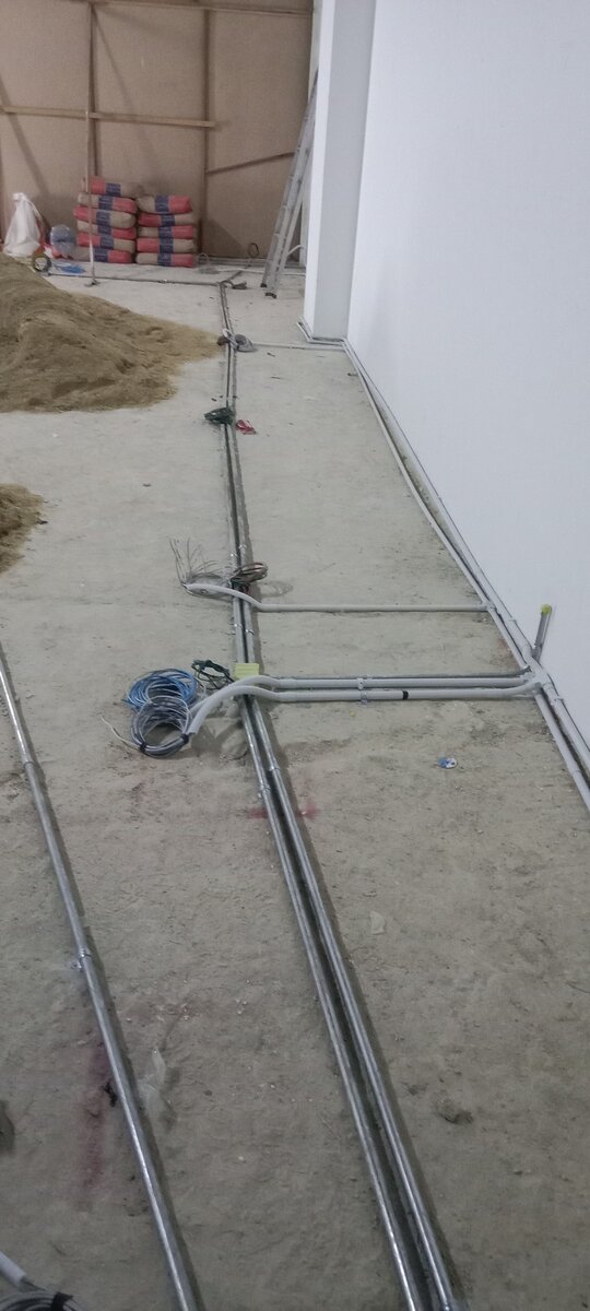 Parallel metal conduit pipes with junctions laid on a cement floor beside a white wall