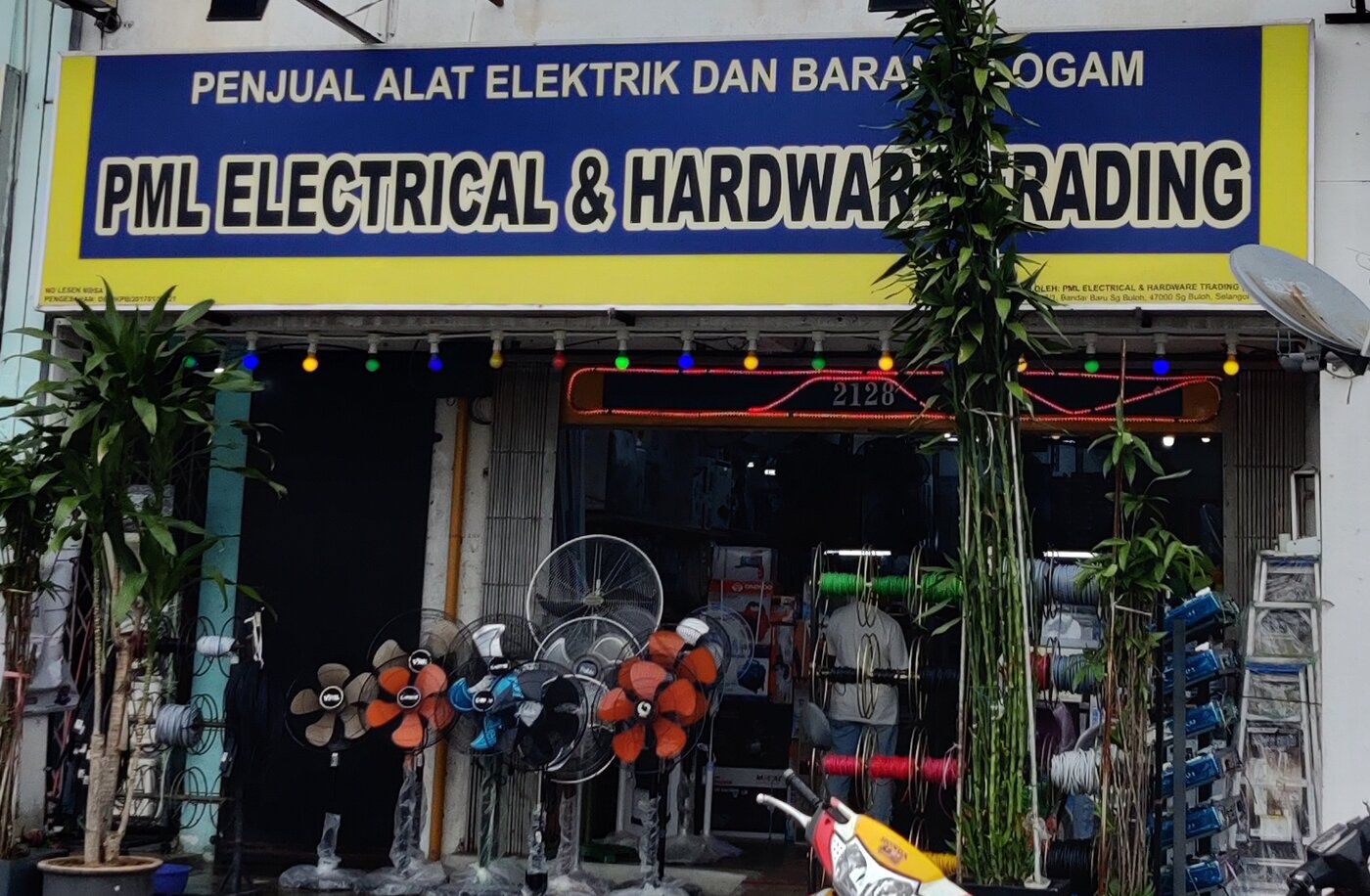 Blue and yellow signboard reading PML Electrical & Hardware Trading above an open shop with a row of stand fans and racks of coloured reels