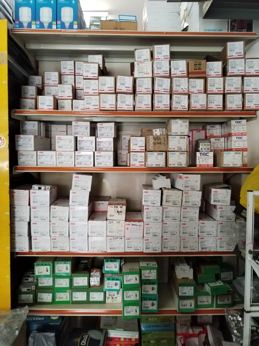 Store shelves stacked with white ABB and Hager boxes, green Schneider Electric boxes and lighting cartons