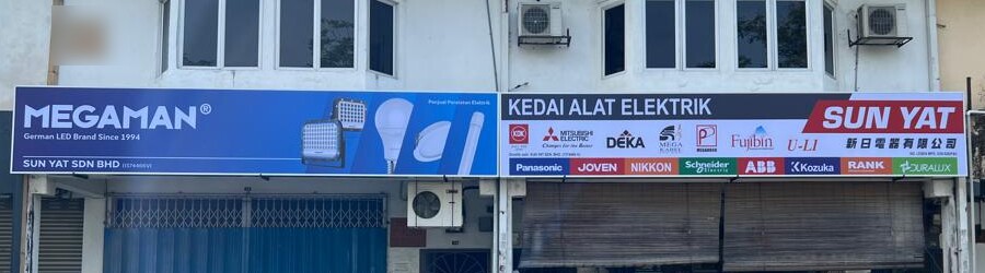 Two shop signboards side by side: a blue Megaman LED sign and a white Kedai Alat Elektrik Sun Yat signboard with two rows of brand logos, above shop shutters