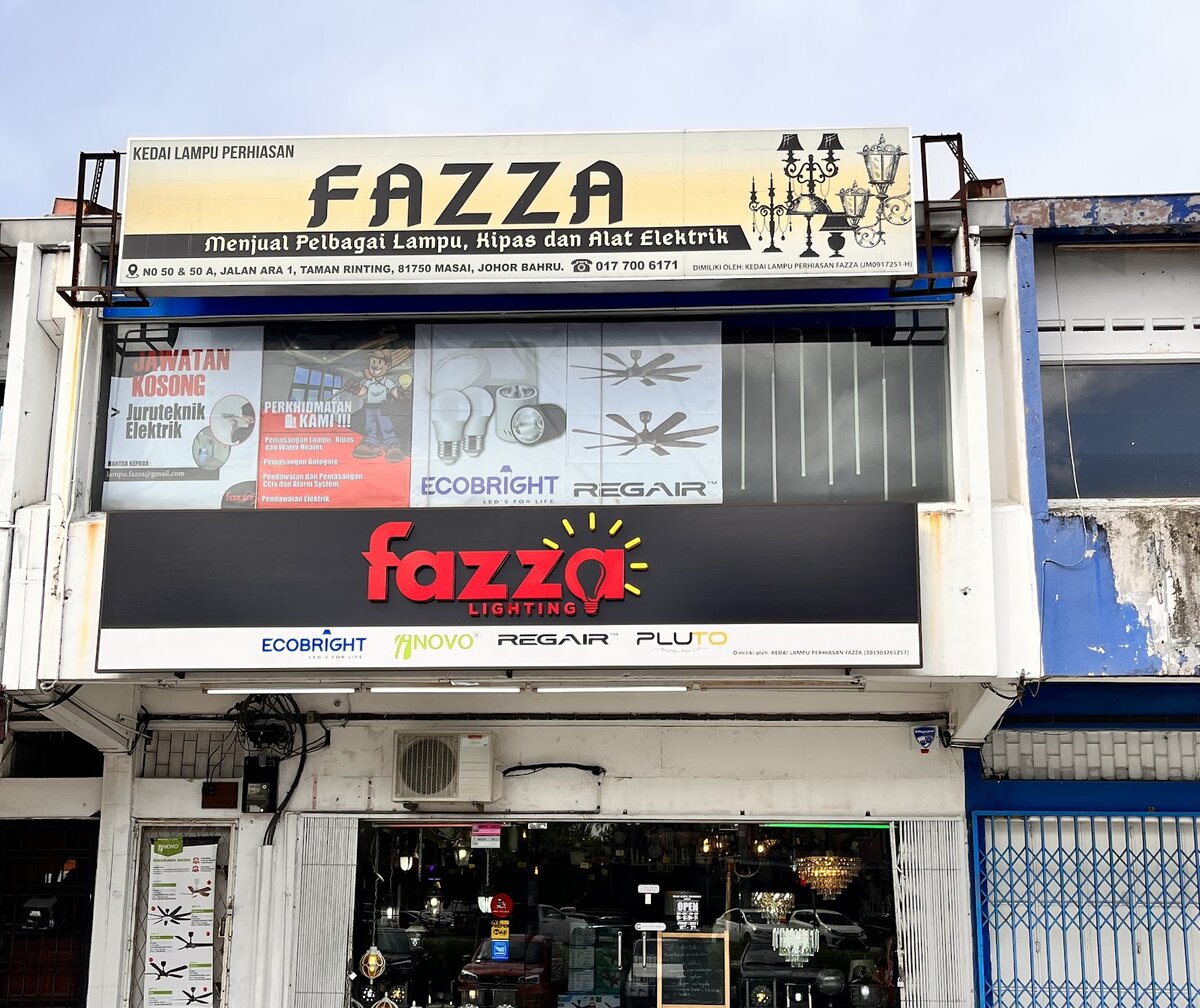 Shophouse with a cream Fazza signboard, window posters for electrical services, Ecobright bulbs and Regair fans, and a red Fazza Lighting sign above the entrance