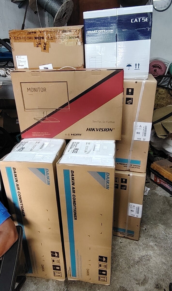 Stacked cardboard boxes labelled Daikin Air Conditioner, a Hikvision monitor box and a Cat 5e cable box