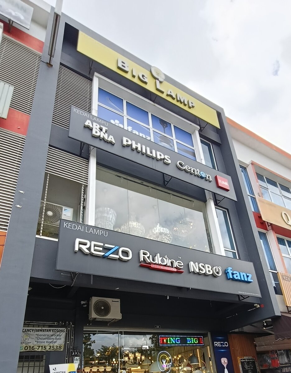 Three-storey shop with a yellow Big Lamp sign and dark signboards showing lighting and fan brands above a lit showroom