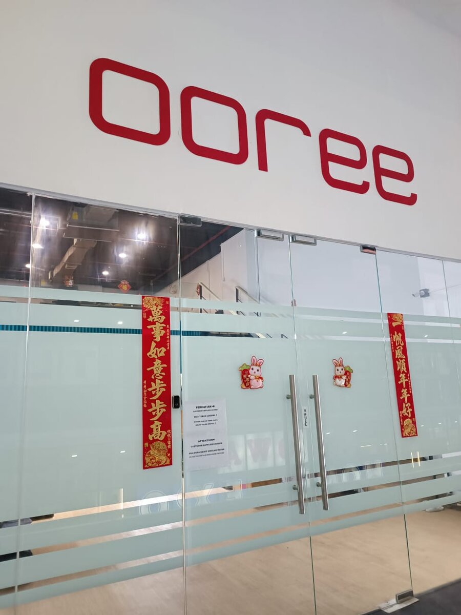Red "ooree" lettering on a white wall above frosted glass doors decorated with Chinese New Year banners