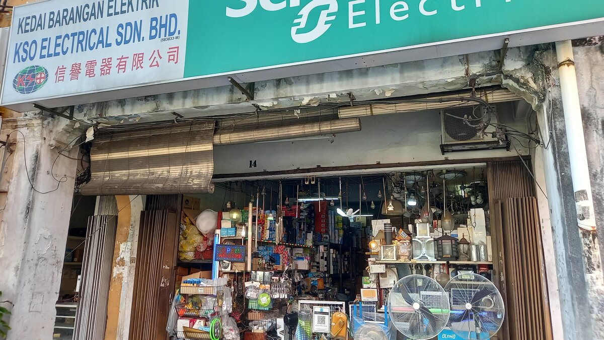 Old shophouse front with a KSO Electrical signboard and Schneider Electric panel, hanging lamps and two large stand fans at the entrance