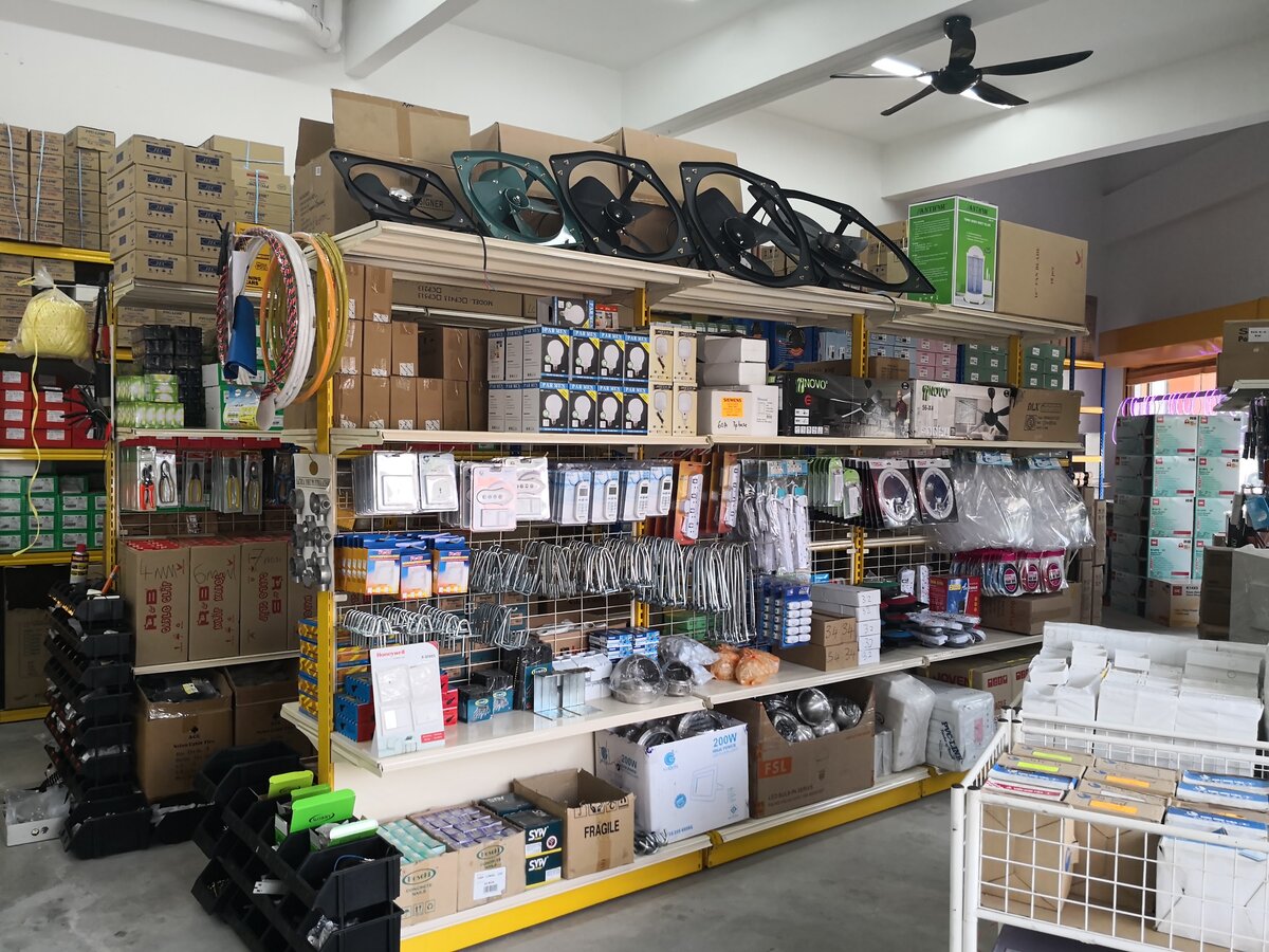 Shop shelving with large black exhaust fans on top, boxed LED bulbs and ceiling fans, pegboards of remote controls, power strips and hooks, and stacked cartons along the walls