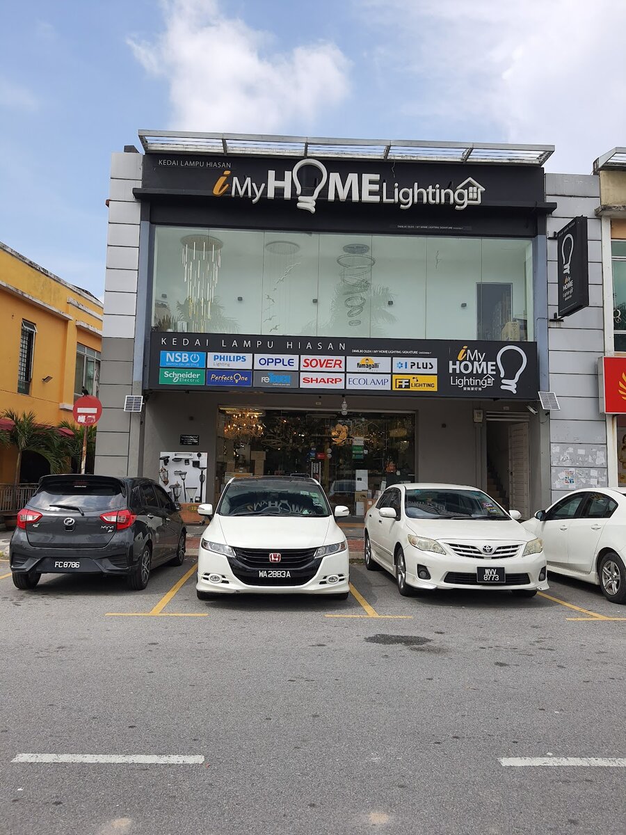 Two-storey shop with a glass front, chandeliers inside and a black signboard of lighting brand logos above the entrance